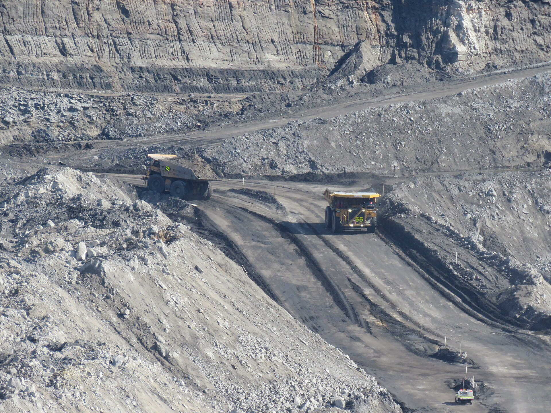 Mining haul trucks travelling through a terraced open pit